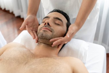 Beyaz adam stres önleyici kafa masajından ve lüks bir tatil beldesi veya otel spa salonundaki modern ışık ortamında yüz güzelliği eğlencelerini şımartmaktan hoşlanıyor. Sessiz.