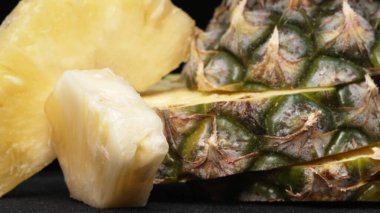 Taze ananaslı ve ayrı siyah arkaplanlı bir ananas dilimli videoyu kapat. Kaba ve balmumu kabuğu, dikenli yeşil yapraklardan bir taç, yemek fotoğrafçılığı. Geliştirilebilir.