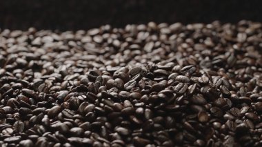 Siyah arkaplanlı taze kahve çekirdeğinin makro çekimi. Etrafı sarılmış aromatik kavrulmuş kahve tohumu yığınlarına yakın. Makrografi. Fasulyeler etrafa saçılıyor. Geliştirilebilir.