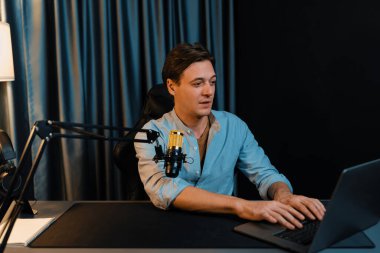 Sunucu kanalı akıllı yayıncı laptopta canlı sosyal medya uygulaması arıyor, kulaklık takıyor ve modern ofis stüdyosundaki mikrofonu kullanıyor. Bireysel.