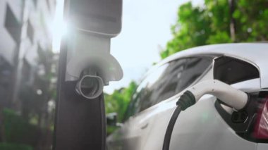 Yavaş çekim EV elektrikli araba yazın yeşil sürdürülebilir şehir bahçesinde şarj oluyor. Kentsel sürdürülebilirlik yaşam tarzı yeşil temiz yeniden şarj edilebilir enerji elektrikli BEV araç iç organları