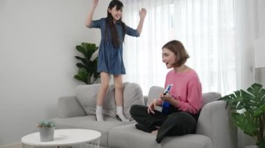 Annem gitar çalıp kıza bakarken yetenekli kız kanepede dans edip zıplıyor. Beyaz anne, çocuk oturma odasında dururken akustik müzik çalar. Aile eğlence konsepti. Pedagoji.