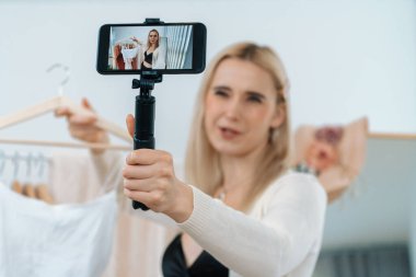 Genç sosyal medyum kadın moda videosu yapıyor. Blogcu gülümseyip telefon çubuğu selfie 'si kullanırken aynı zamanda ikna edici online giysiler izleyicilere ya da takipçilere vlog sattırıyor. Blithe