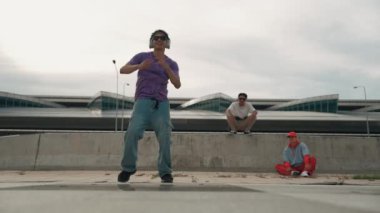 Bir grup Asyalı break dansçı, çok kültürlü arkadaş desteği ve hareketli hip hop müziğiyle sokak dansı yaptılar. Çekici yakışıklı hippi sokak dansında break dansçı. Açık hava sporu 2024. Yumuşak bir şekilde..
