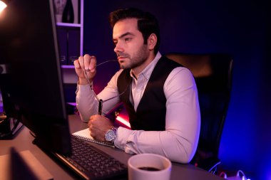 Stresli akıllı işadamı, kağıt işleri üzerine not pazarı verileri yazarak, gece geç saatlerde mor neon karanlık aydınlatma odasındaki disiplin ürünü hizmetlerinin çevrimiçi satış kanalını analiz ediyor. Tahmin et..