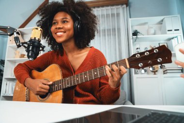 Genç Afrikalı Amerikalı müzisyenin sunucu kanalı gitar çalıyor, şarkı söylüyor, stüdyoda dizüstü bilgisayardan yayın yapıyor. Kulaklık dekorasyonu ve mikrofon kaydı. Tatlandırıcı.
