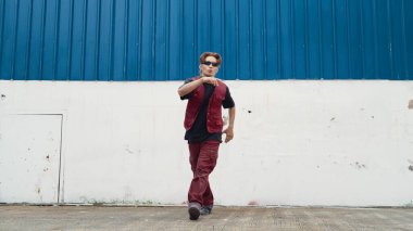 Beyaz arka planda break dans pratiği yapan yakışıklı bir sokak dansçısı. Hip hop tarzı giyinen sporcu, mavi arka planlı bir sokakta müzik eşliğinde ayak sesleri çıkarıyor. Açık hava sporu 2024. ÇalışmaComment.