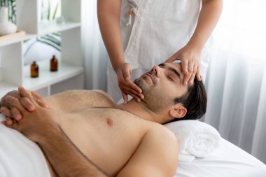 Beyaz adam stres önleyici kafa masajından ve lüks bir tatil beldesi veya otel spa salonundaki modern ışık ortamında yüz güzelliği eğlencelerini şımartmaktan hoşlanıyor. Sessiz.