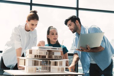 Yetenekli mimarın portresi dizüstü bilgisayarı tutarken mühendis ekibine sundu. Bir grup iş adamı beyin fırtınası ve bina inşaatı yapıyor. İnşaat mühendisliği, birlikte çalışıyoruz. İzleme.