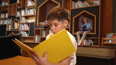 Bir grup zeki öğrenci kütüphanede otururken beyaz çocuk kitap okuyor. Çekici çocuk ders çalışıyor, çocuklar konuşurken romandan ya da kitaptan öğreniyor, eğitim hakkında sohbet ediyor. Etkinlik.