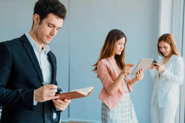 Kitap okuyan ve iş yerinde iş arkadaşları ve arkadaşlarıyla çalışan genç ve yakışıklı bir işadamı. Kurumsal iş adamları grubu. uds