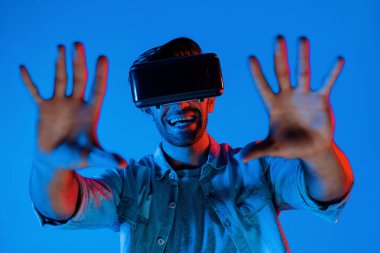 Heyecan verici bir sporcu el hareketi yaparken VR gözlüğü takıyor. Yetenekli genç ayakta duruyor ve teknolojik yenilikleri kullanarak gelecekteki sanal dünya programını veya metaevreni inceliyor. Sapma.