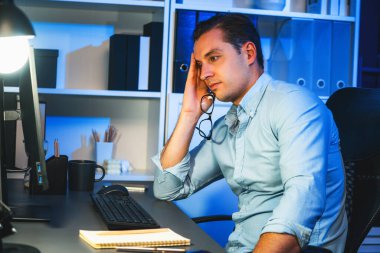 Çalışan bir işadamı, gece vakti projesiyle uykulu bir şekilde e-posta bilgilerinin modern işyerine gönderilmesini bekliyor. Uzaktan kumandalı çevrimiçi çalışmadan zaman içinde sıkılan serbest çalışan teması. Satılabilir.