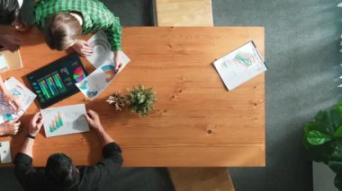 Akıllı iş adamlarının yukarıdan görünüşü toplantıda verileri analiz eder. Birlikte çalışan bir grup iş adamı ve toplantı masasına yerleştirilen tabletin mali tablosuna bakıyorlar. Cemaat.