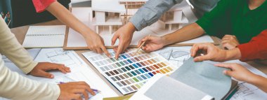 Yetenekli mimar takımı ev inşaatı hakkında tartışırken, iç mimar ev modeli ve bina planının dağıldığı renk paletine uygun bir renk belirliyor. Üst Manzara. Değiştirilmiş.