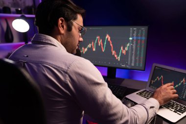 Akıllı tüccar işadamı, karanlık oda gecesinde neon ışıklı ofisteki arama pazarında yüksek kârla ekranda bilgisayar ve bilgisayar üzerinde dinamik borsa yatırımları üzerinde yoğunlaşıyor. Tahmin et..