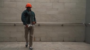 Asyalı akıllı hipster, kulaklık ve şık kıyafetler giyip hip hop şarkıları dinlerken gri arka planlı enerjik break dans gösterisi yapıyor. Açık hava sporu 2024. Hip hop hareketi. Yumuşak bir şekilde..