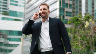 Başarılı bir iş adamı, pazarlama ekibiyle telefon kullanarak yatırım hakkında konuşurken çatıda duruyor. Kafkasyalı yatırımcı modern gökdelen manzarasına bakarak rahatlamanın keyfini çıkarıyor. Yaşam tarzı. Urbane