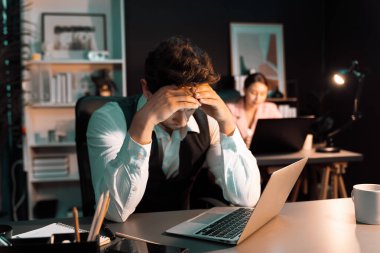 Ciddi yüzü olan bir adam modern ofiste gece aydınlatma zamanı yaratıcı proje planlaması yapıyor bulanık sekreterle birlikte klasör arkaplan konseptiyle kağıt raporlarını kontrol ediyor. Varsayım.