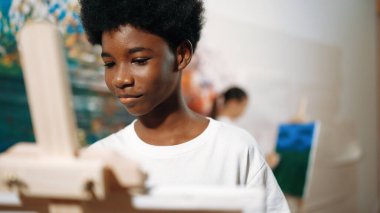 Afrikalı erkek tuvali sıcak tonda boyarken, beyaz elbiseli kız renkli duvarın arkasında havalı renkler çiziyor. Yaratıcı aktivite konsepti. Öğretim.