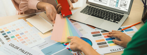 Cropped image of interior designer chooses color from color swatches while laptop displayed website wireframe designs for mobiles app and website. Creative design and business concept. Variegated.