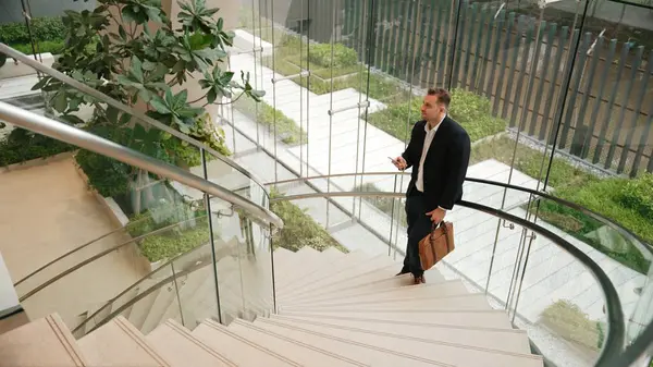 stock image Caucasian businessman analyzing marketing data from mobile phone and making decision at modern glass wall building. Happy project manager checking start up project sales report while standing. Urbane