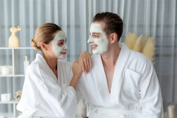 stock image Blissful couple in bathrobe with facial cream mask enjoying serene ambiance of spa salon resort or hotel during holiday. Pampering face spa and skincare treatment with essence relaxation. Quiescent