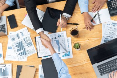 Toplantı odasında iş arkadaşıyla tokalaşan iki işadamı neşeli bir alkış veriyor. Analistlerden oluşan ekip, iş stratejik performansında kaydedilen önemli ilerlemeyi kutluyor. Çok titiz.