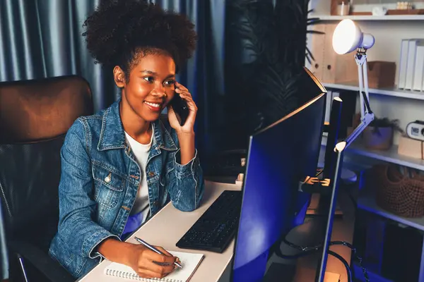 stock image Young African creator calling with smartphone and looking on screen monitor laptop, wearing jeans shirt. Getting project or study new technology at workplace. Theme of teenager winning. Tastemaker.