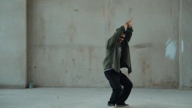 Hippi, şehir caddesinde hip-hop dinlerken kulaklık takıyor. Sokak dansçısı ayak seslerini kulaklıktan müziğe taşıyor. Açık hava sporu 2024. Çimento arka planı. Moda. Aktif stil. hiphop.