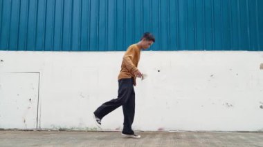 İspanyol adam kollarını açıp duvarın önünde dans ediyor. Dansçı ya da koreografın günlük kıyafetleriyle hip hop tarzında break dans yaparken ki görüntüsü. Açık hava sporu 2024 hiphop..