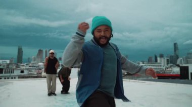 Çok kültürlü veya çok kültürlü hipster grupları şık ve renkli giysiler giyerek çatıda şehir manzaralı ve gökyüzü kazıyıcılarıyla dans ederler. Canlı sokak dansı konsepti. Açık hava sporu 2024 hiphop..