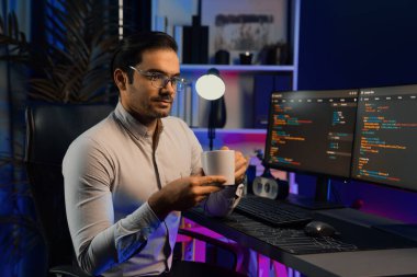 Akıllı IT geliştiricisi, bilgisayar ekranında yazılım geliştirme kodlu kahve fincanı tutuyor. Dışarıya bakıyor, program güncellemesi internet sitesi verilerini neon ışıklı siber ofiste sunuyor. Tahmin et..