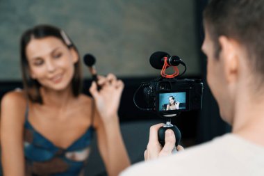 Genç bir kadının sosyal medya için güzellik ve kozmetik dersi videosu çekmesini videoya çeken bir adam. Güzellik blogcusu kameraya gülümserken seyircilere ve takipçilere güzellik bakımını gösteriyor. Açılıyor