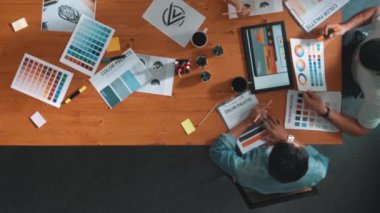 Proje yöneticisi renk paletleri seçerken tasarımcının tablete baktığı yukarıdan aşağıya hava görüntüsü. Profesyonel grafik tasarımının en üst görüntüsü ve logoya bakın. Yetenekli ekip grafikleri seçiyor. Sempozyum.