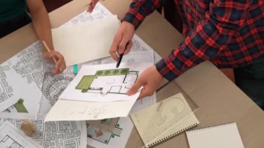 Mimari döküman, ölçüm araçları ve ahşap blokların modern ofiste etrafa saçıldığı masa üzerine planlar yapma konusunda akıllı mimar ve güvenlik mühendisi tartışması. - Yakın çekim. Tanımlama.