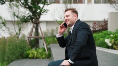 Akıllı beyaz iş adamı akıllı telefona bakıyor ve raporları kontrol ediyor. Çevre parkında ya da şehir merkezinde otururken pazarlama planı hakkında konuşurken ya da müdürle konuşurken gülümseyen mutlu yatırımcı. Urbane.