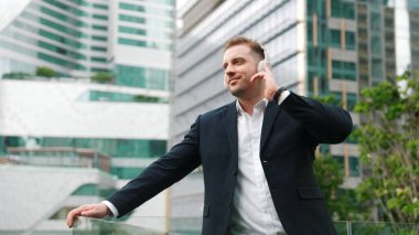 Erkek liderin etrafını sarın kulaklığı dinleyin ve neşeli ve motive edici bir şekilde rahatlatıcı müzikle dans edin. Becerikli proje yöneticisi şehir merkezinde akıllı telefon kullanırken rahat şarkılar dinlemeyi sever. Urbane.