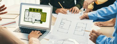 Profesyonel mimar, mimari dökümanlar etrafa saçılmışken toplantı masasındaki planların değiştirilmesiyle ilgili tartışmalarda çevre dostu evin planına karar veriyor. - Yakın çekim. Tanımlama