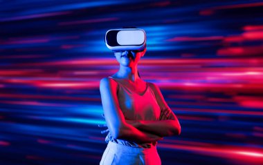 Zeki bir kadın, metaevreni birbirine bağlayan VR kulaklık takan neon ışıklarla çevrili duruyor. Gelecekteki siber uzay topluluğu teknolojisi. Zarif kadın kendinden emin bir şekilde çapraz kol pozu veriyor. Uzağa bak. Halüsinasyon.