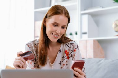 Genç mutlu kadın internetten alışveriş yaparak ürün satın alırken aynı zamanda internet üzerinden online ödeme sistemi ile çevrimiçi mağaza platformundan en yüksek siber güvenlik tarafından korunan ürünler sipariş ediyor.