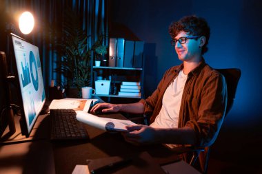 Genç işadamı, Neon Light Modern Ofis 'teki yeni proje surround çalışma masası için kağıt üzerinde tasarım düşünüyor. E-posta ile hediye göndermeden önce not defterine yeni bir iş düşünüyorum. Toplayıcı.