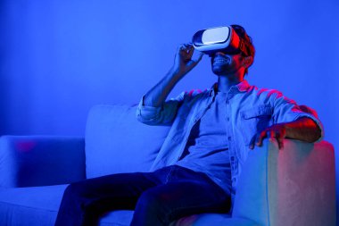 Adam film izlemek ve kanepede neon ışıkla oturmak için metaevrene girmek için VR camına bakıyor. Kafkasyalı ergen günlük giysiler giyiyor ve sanal gerçeklik simülasyonu programı takıyor. Sapma.