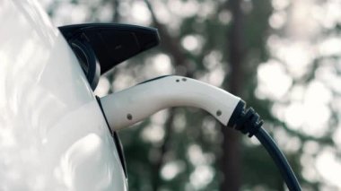 Doğal yeşil şehir parkındaki otoparkta EV elektrikli araba şarj pili. Sürdürülebilir ve çevre dostu şehir yolculuğu için yenilenebilir otomobil için alternatif temiz enerji teknolojisi. Titiz