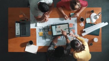 İnşaat mühendislerinin masa başında proje planıyla otururken tablet kullanarak ev yapısını dizayn etmelerine tepeden aşağı bir bakış açısı. Ekip planlama ve inşaat hakkındaki fikirlerin havadan görüşü. Sempozyum.