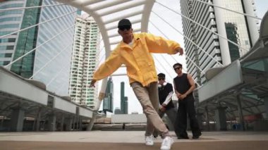Kameraya bakarken mutlu hipster dansının düşük açılı kamerası. Sokak dansçısı şehirde arkadaşlarıyla birlikte break dans yapıyor. Serbest stil dansı. Açık hava sporu 2024. Yumuşak bir şekilde..