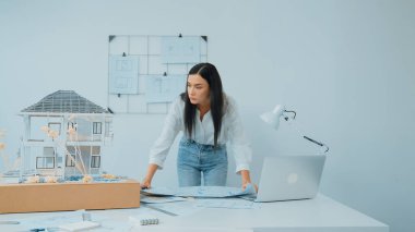 Genç, güzel beyaz bir mimar masanın üzerine plan koyar ve ev modeliyle karşılaştırırken, modern ofisteki fahişe modellerini dikkatlice incelerken arkadaki çizgilerle karşılaştırır. Tertemiz..