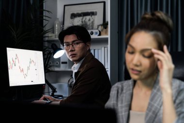 Stresli iş kadını, arka planda çalışan iş arkadaşıyla e-posta yoluyla bilgisayar borsasına bakıyor. Akşamları modern ofis binasında zarar karıyla ilgili soru sormak için konuşuyorlar. İnfobahn.