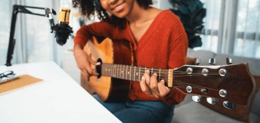 Genç Afrikalı Amerikalı müzisyenin sunucu kanalı gitar çalıyor, şarkı söylüyor, stüdyoda akıllı telefondan yayın yapıyor. Ekipman kulaklıkları dekorasyonu ve mikrofon kaydı. Tatlandırıcı.