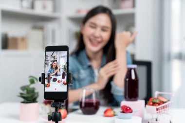 Seçici odaklı akıllı telefon ve gülümseyen genç, güzel Asyalı karışık çilek ve kiraz suyu detoksu değerlendirmesi sosyal medyada sağlıklı ürün tanıtımı sunuyor. Taktik.